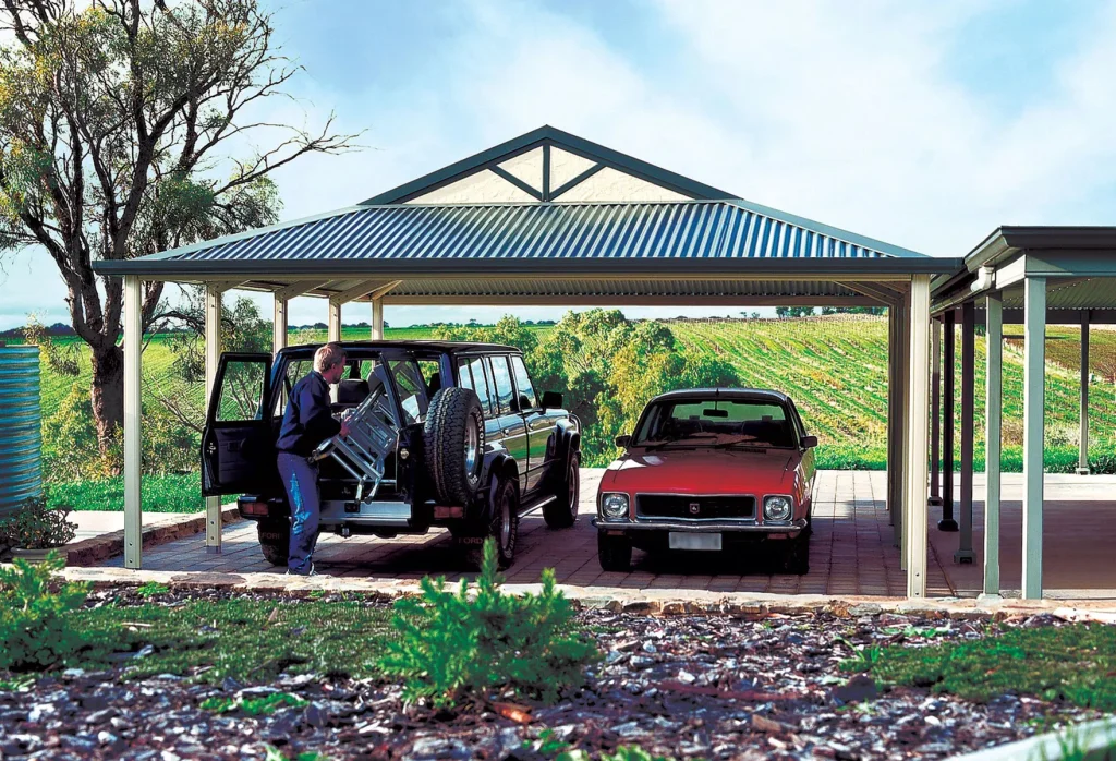 Two cars parked under metal carport in countryside.