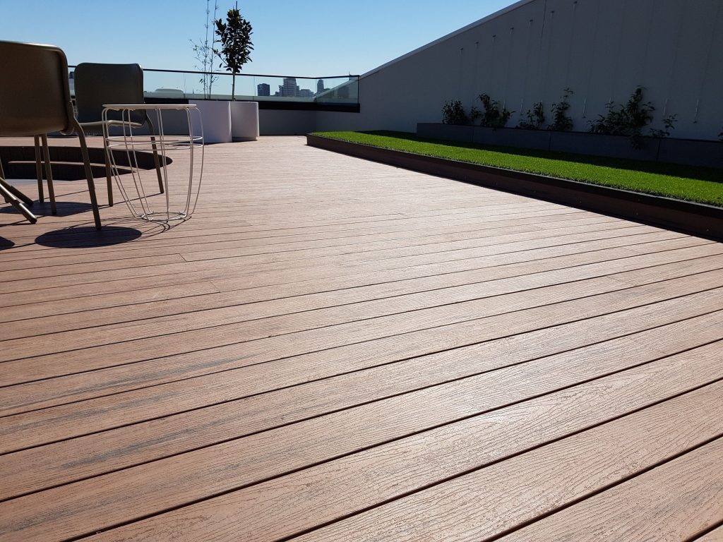 Sunny rooftop terrace with wooden flooring and chairs.