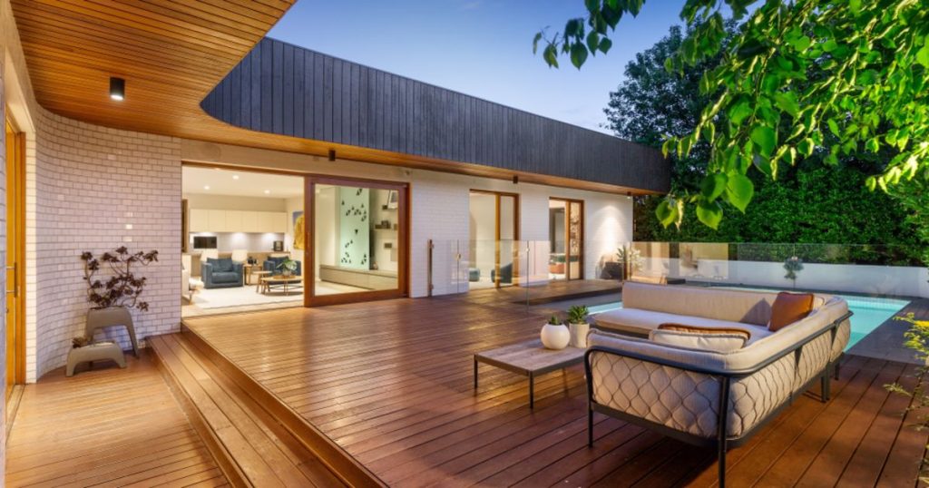 Modern patio with wooden deck, pool and seating area.