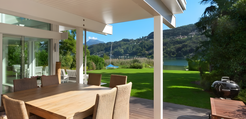 Lakeside patio with garden view and wooden furniture.